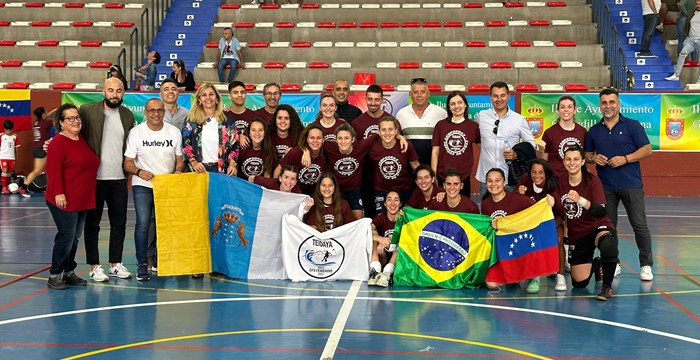 El equipo del CFSF Teidaya Arico celebrando su clasificación para la Segunda División femenina de Fútbol Sala junto a sus entrenadores y seguidores, mostrando banderas representativas.